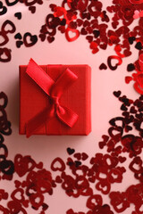 Small red giftbox and heart confetti on pale pink background. Flat lay.