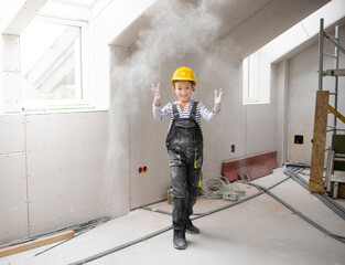 cool young boy with yellow safety helmet posing and having fun on construction building site indoor in a loft