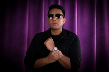 Young modern latin man portrait while he hold his hands together as a confident and powerful man posing. He is standing over a purple background