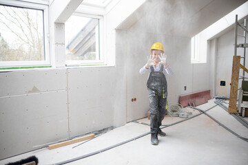 cool young boy with yellow safety helmet posing and having fun on construction building site indoor in a loft