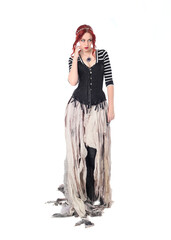 full length portrait of girl with red hair wearing black corset , torn gothic fantasy gown and leather boots. standing pose, isolated on white studio background.