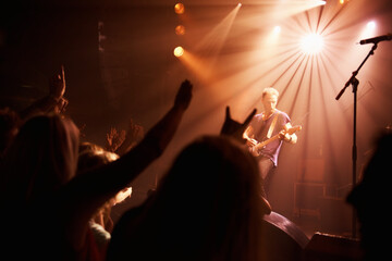 Rear view of an excited crowd cheering their favourite band on beneath the strobe lights at a...