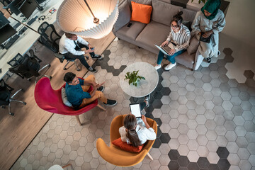 Top view photo of Multiethnic startup business team having brainstorming in relaxation area of modern office interior working on laptop and tablet computer