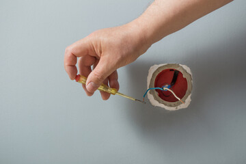 The electrician inserts a tester screwdriver into the hole of the socket to determine the phase wire