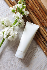 Fototapeta na wymiar Mockup of white squeeze bottle plastic tube for branding of medicine or cosmetics - cream, gel, skincare. Cosmetic bottle container, matthiola flowers and reeds on wooden table.