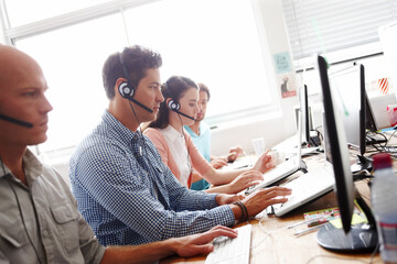 Servicing their clients. Sales assistants at the office working in front of their computers wearing headsets.