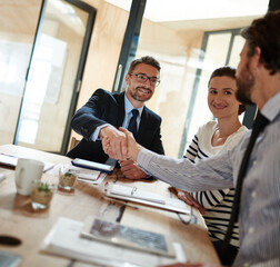 Making deals in the boardroom. Shot of two businesspeople shaking hands in an office while a...