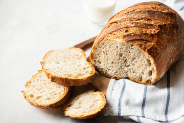 Homemade artisanal sliced sourdough bread on a napkin and glass of milk on a gray background. Healthy home baking concept.