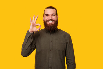 Bearded man is showing ok gesture. Studio shot over yellow background.