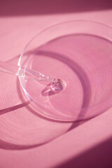 Dropper pipette with serum or cosmetic liquid and petri dish on pink background. Transparent container with liquid and bubbles. The appearance of the texture of the gel. Medicine and beauty concept.