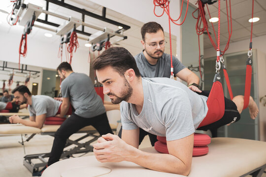  Rehabilitation specialist performing active treatment on suspension straps for female patients. Concept of therapeutic exercises to restore pain-free movement patterns and improve function