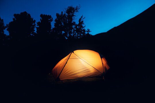 An Orange Tent Illuminated By A Headlamp At Night In The Forest. Camping And Hiking At Twilight. Lighting Equipment At Trekking Trip