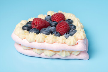 Pavlova meringue cake decorated with fresh raspberry and blueberry berries on blue background, close up