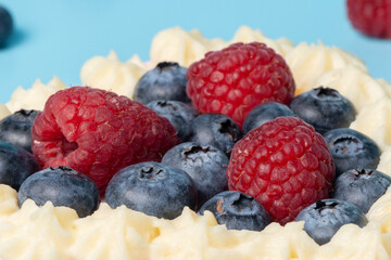 Pavlova meringue cake decorated with fresh raspberry and blueberry berries on blue background, close up