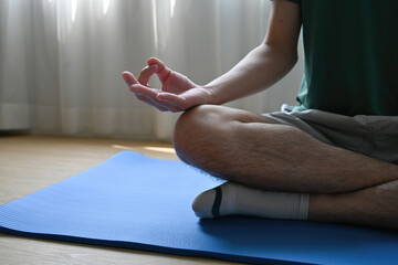 Cropped view a man sitting cross-legged meditating on a mat in a living room or yoga studio, for home exercise , meditation and yoga concept.