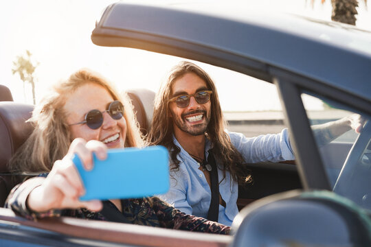 Young couple having fun doing selfie inside convertible car during summer vacation - Travel concept - Focus on man face