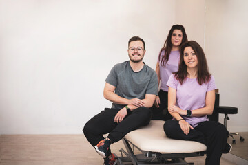 a group of three physiotherapists posing on a stretcher in their clinic room.Copyspace