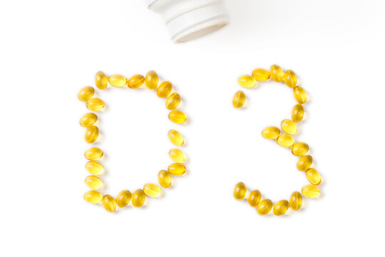 Yellow oil capsules with vitamin D poured from a plastic white bottle and forming shape D3 on the white background. - Image