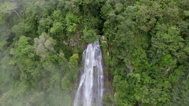 Aerial pan left of Las Lajas waterfall streaming down a high cliff surrounded by dense green rainforest, San Luis Morete, Costa Rica