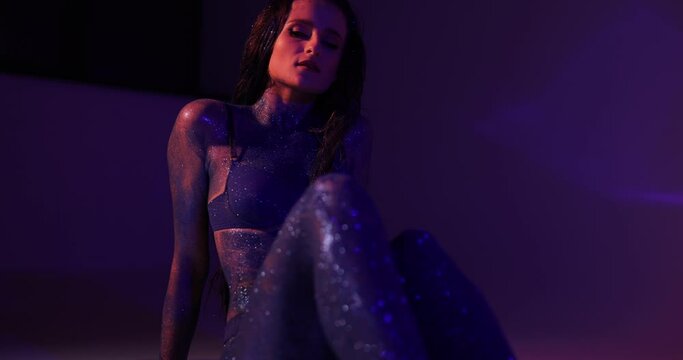 Attractive woman with blue glitter on the body posing sitting in a studio