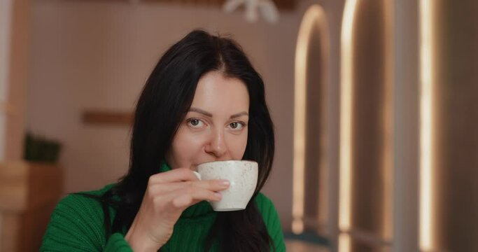 Woman drinks coffee sitting at the table in cafe