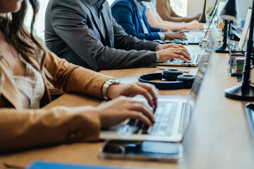 Close Up Photo of Business People Hands Using Laptop Computers at Office Desk.

Unrecognizable team of five businessman and businesswoman sitting in a row at same table and typing report on keyboard.