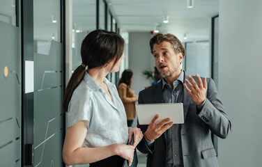 Serious Businessman Holding Digital Tablet and Talking with his Anonymous Female Colleague at Work....