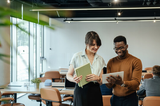 Happy Businesswoman and Businessman Using Digital Tablet Together at Work. 

Two smiling colleagues analyzing business report on a tablet while unrecognizable multi-ethnic team working at desk.