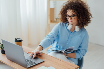 Young curly woman work on the notebook, drink coffee and talk on the phone