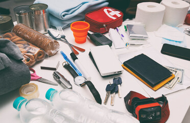 Emergency backpack equipment organized on the table. Documents, water,food, first aid kit and another items needed to survive.