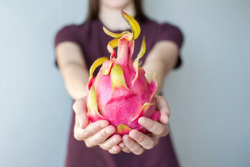 girl holding dragon fruit pitahaya in her hands close up on a gray background