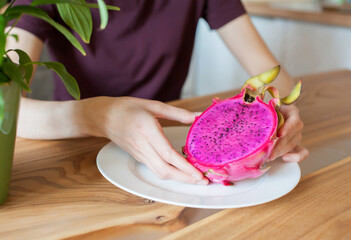 The girl holds in her hands a cut dragon fruit pitahaya at home in the kitchen close-up. soft focus