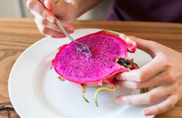 Girl with a spoon eats dragon fruit pitahaya at home in the kitchen close-up. defocus