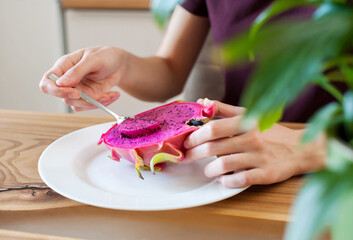 Girl with a spoon eats dragon fruit pitahaya at home in the kitchen close-up