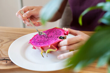 Girl with a spoon eats dragon fruit pitahaya at home in the kitchen close-up