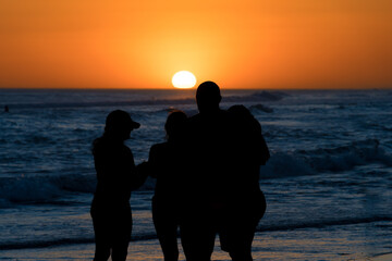 Silhouettes of people in front of a colorful sunset on the beach.