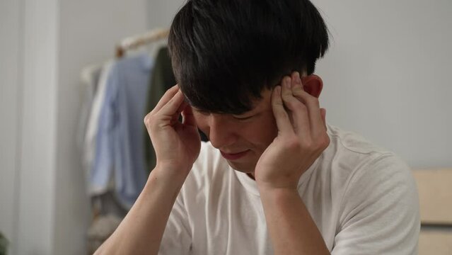 closeup view of a sick asian man waking up with hangover is trying to relive bad headache by massaging in the bedroom at home