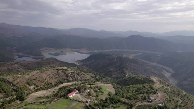 Front drone video in "golden hour" advancing over the mountains of SH22 in albania, over the village of Va Spas and in the background Lake Drin. the cloudy letting the sun's rays through.
