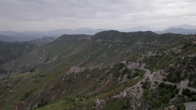 "golden hour" head-on drone video moving over the mountains of SH22 in albania, above the road on top of the hill. Cloudy sky and some small houses can be seen.