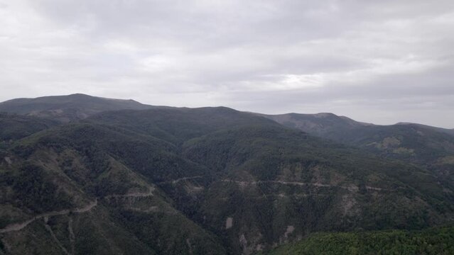 "golden hour" head-on drone video moving over the mountains of SH22 in albania, above the road on top of the hill. Cloudy sky and some small houses can be seen.