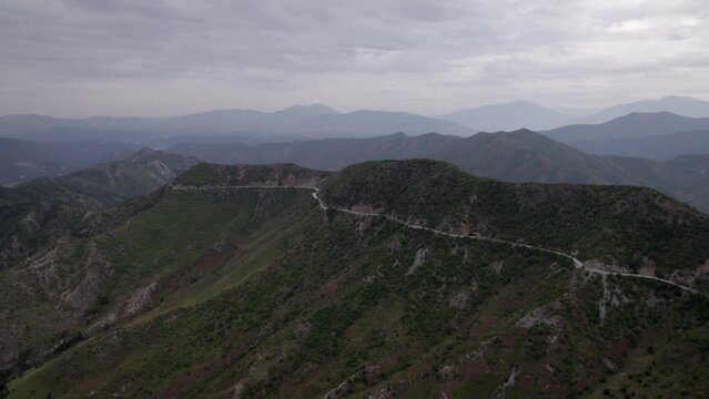 "golden hour" head-on drone video moving over the mountains of SH22 in albania, above the road on top of the hill. Cloudy sky and some small houses can be seen.
