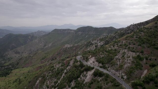 "golden hour" head-on drone video moving over the mountains of SH22 in albania, above the road on top of the hill. Cloudy sky and some small houses can be seen.