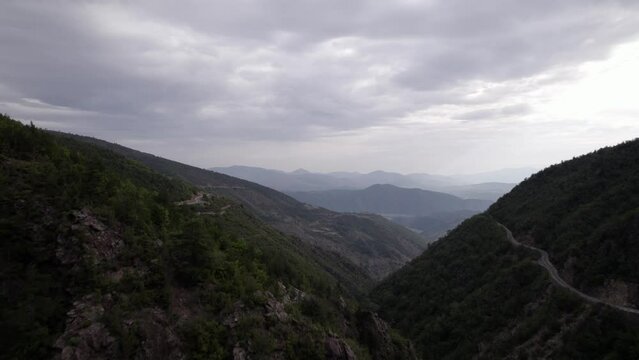 Frontal drone video ascending in "golden hour" discovering the mountains of SH22 in albania, over the town of Va Spas and in the background Lake Drin. cloudy sky letting the sun's rays through.