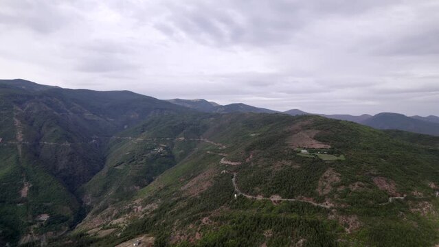 "golden hour" head-on drone video moving over the mountains of SH22 in albania, above the road on top of the hill. Cloudy sky and some small houses can be seen.