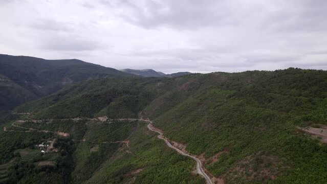 "golden hour" head-on drone video moving over the mountains of SH22 in albania, above the road on top of the hill. Cloudy sky and some small houses can be seen.