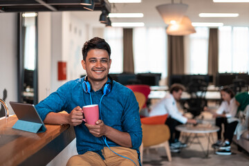 Casual business man taking break from the work using laptop while drinking tea in relaxation area of modern open plan startup office