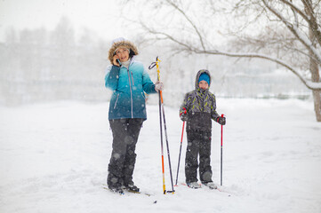 A boy with a woman learns to ski while walking in a snowfall. Outdoor activities for children in winter. Physical education lessons. - 488979972