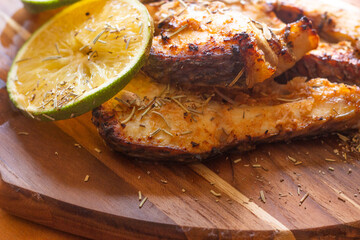 close up of .fried fish slices with orange and rosemary on wooden table