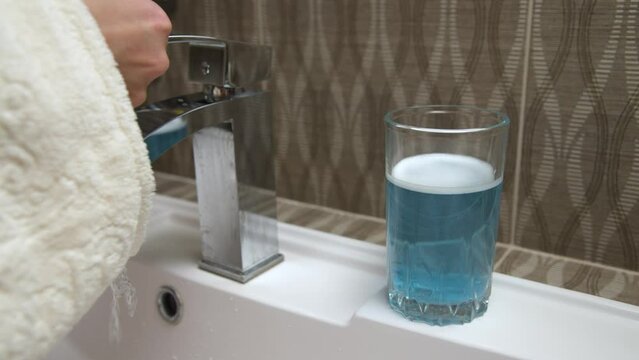 Close-up of washing a polymer aligner in a glass of cleaning solution of water. The hands of a caucasian woman put an aligner to correct an overbite in glasses