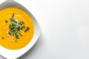 Pumpkin cream soup with green onion and pumpkin sesame seeds in white soup plate. Isolated on white background. Copy space. Vegetarian vegetable healthy food.